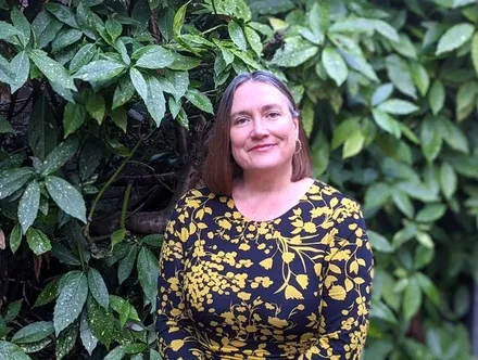 Julie Bentley smiling outdoors in front of leafy greenery